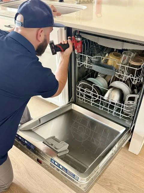 Technician using a power driver beside an open dishwasher